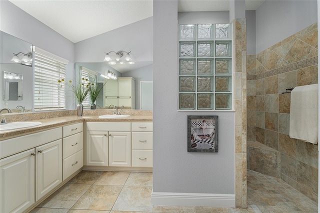 bathroom with tile patterned flooring, vaulted ceiling, tiled shower, and vanity