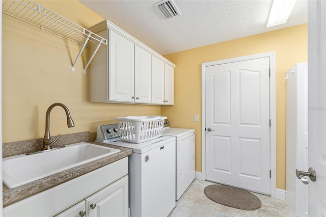 washroom with light tile patterned flooring, sink, washing machine and clothes dryer, a textured ceiling, and cabinets