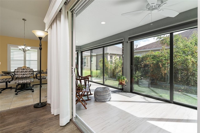 sunroom / solarium featuring ceiling fan with notable chandelier and a wealth of natural light