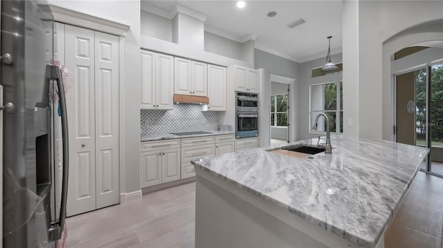 kitchen with light stone counters, sink, a center island with sink, white cabinetry, and appliances with stainless steel finishes