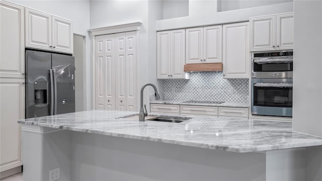 kitchen with appliances with stainless steel finishes, sink, light stone counters, and white cabinetry