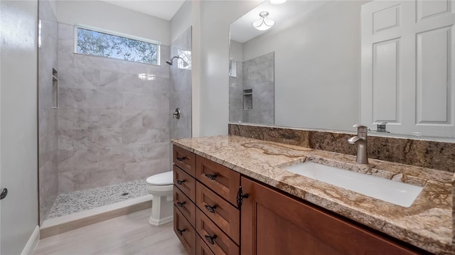 bathroom featuring wood-type flooring, tiled shower, vanity, and toilet