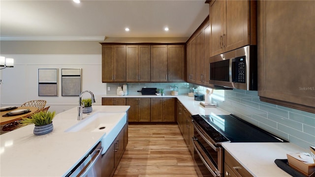 kitchen with sink, light hardwood / wood-style flooring, backsplash, appliances with stainless steel finishes, and crown molding