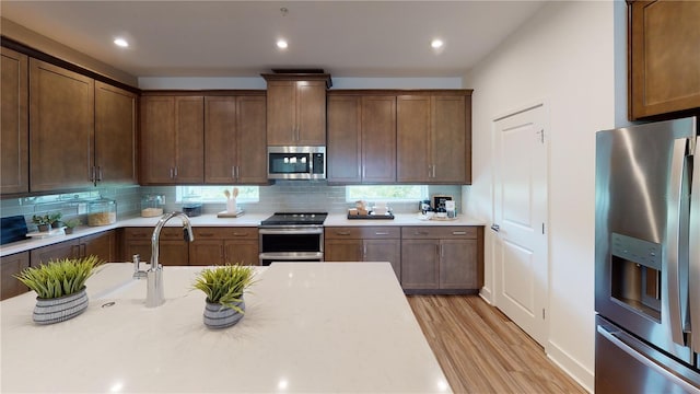 kitchen with decorative backsplash, light hardwood / wood-style floors, appliances with stainless steel finishes, and sink