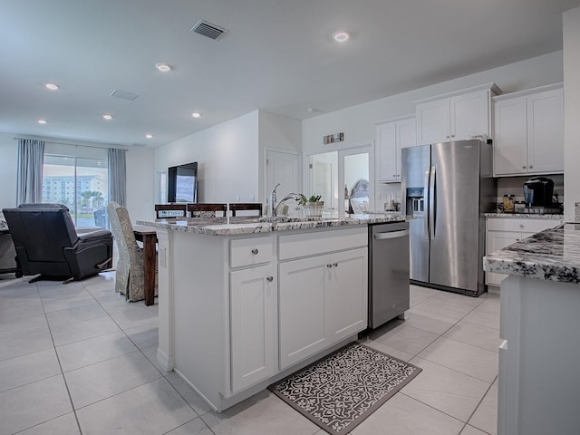 kitchen with light stone countertops, appliances with stainless steel finishes, white cabinetry, and an island with sink