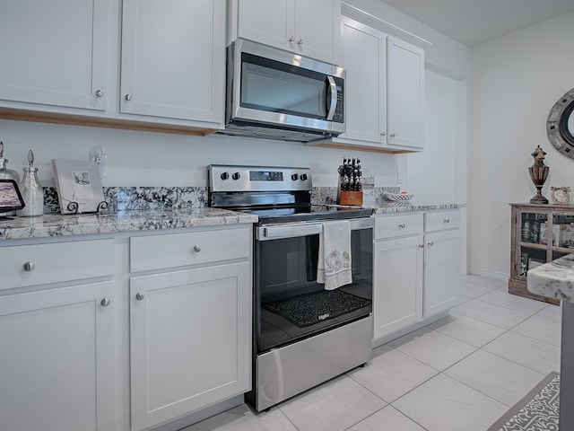 kitchen with light tile patterned floors, light stone countertops, white cabinetry, and appliances with stainless steel finishes