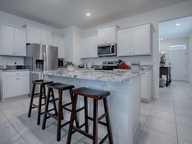 kitchen with light tile patterned floors, an island with sink, a breakfast bar area, white cabinets, and appliances with stainless steel finishes