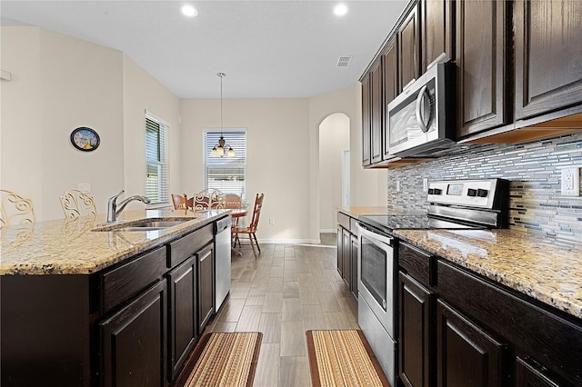 kitchen featuring a center island with sink, sink, appliances with stainless steel finishes, tasteful backsplash, and decorative light fixtures