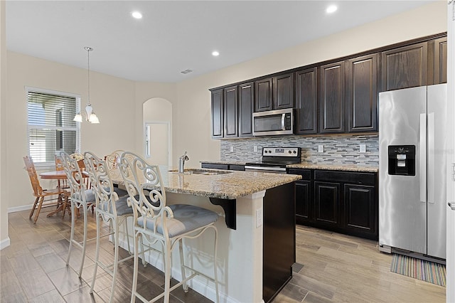 kitchen featuring sink, hanging light fixtures, stainless steel appliances, a breakfast bar area, and a kitchen island with sink