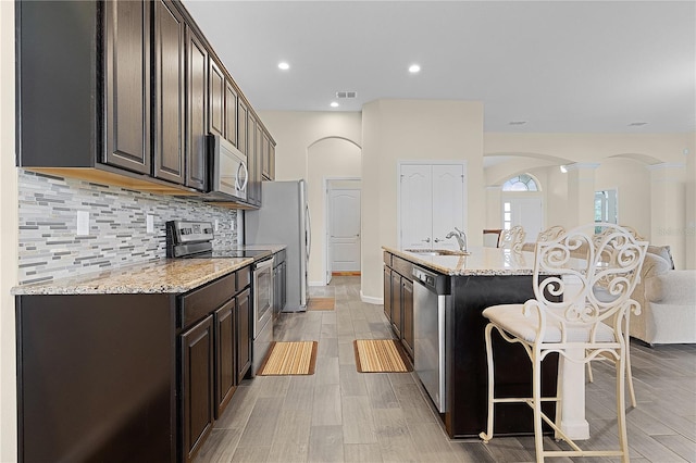 kitchen featuring light stone counters, a breakfast bar, stainless steel appliances, light hardwood / wood-style floors, and an island with sink