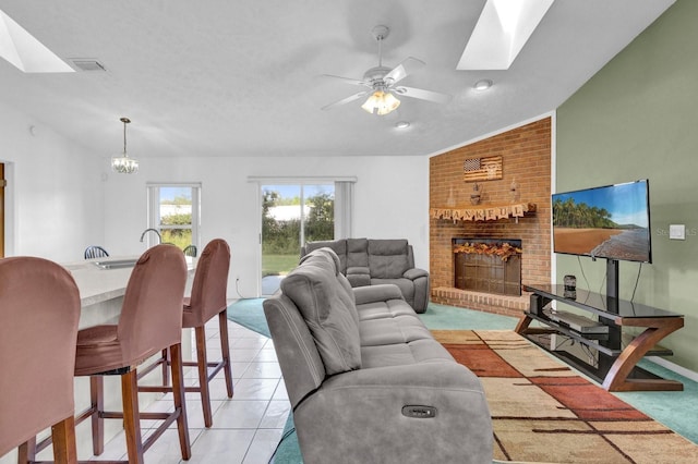 tiled living room featuring vaulted ceiling with skylight, a fireplace, and ceiling fan with notable chandelier