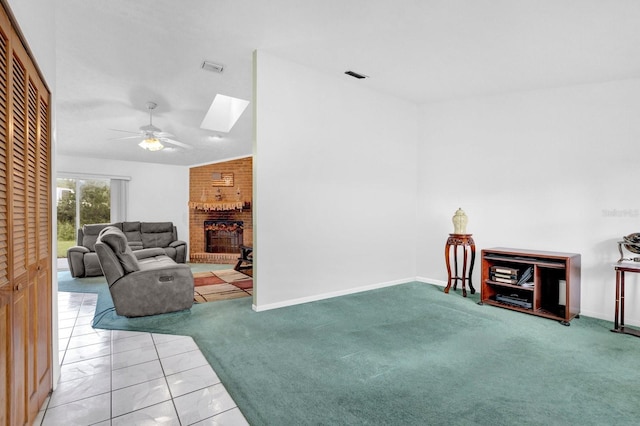 interior space featuring ceiling fan, a brick fireplace, tile patterned flooring, and a skylight