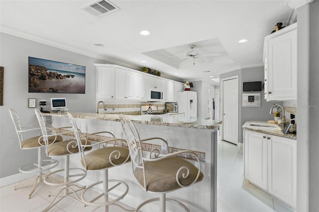 kitchen with white cabinets, ceiling fan, crown molding, light stone counters, and white appliances