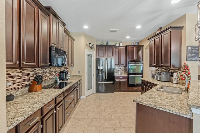 kitchen with sink, decorative backsplash, light stone countertops, black appliances, and a textured ceiling