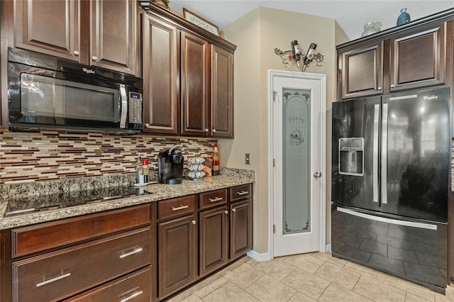 kitchen with black appliances, light stone countertops, dark brown cabinets, light tile patterned floors, and backsplash