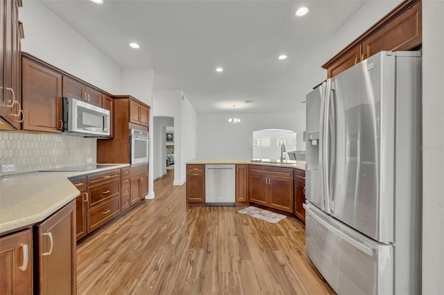 kitchen with kitchen peninsula, decorative backsplash, appliances with stainless steel finishes, light wood-type flooring, and sink