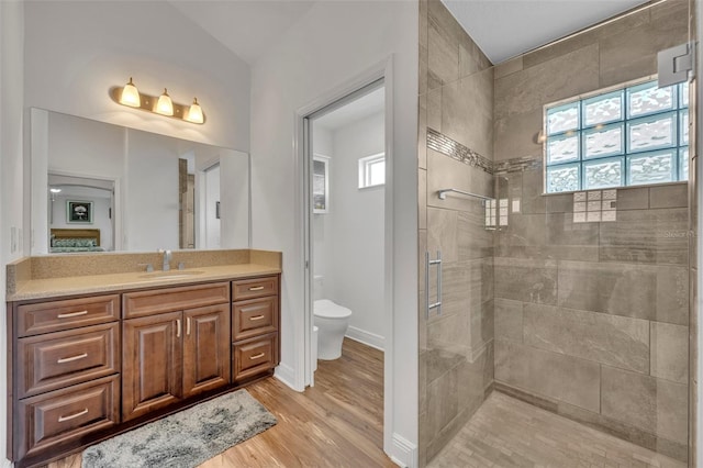 bathroom featuring vanity, a tile shower, hardwood / wood-style flooring, and toilet