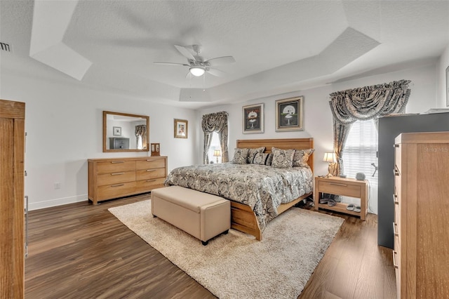 bedroom with dark hardwood / wood-style flooring, a textured ceiling, a tray ceiling, and ceiling fan