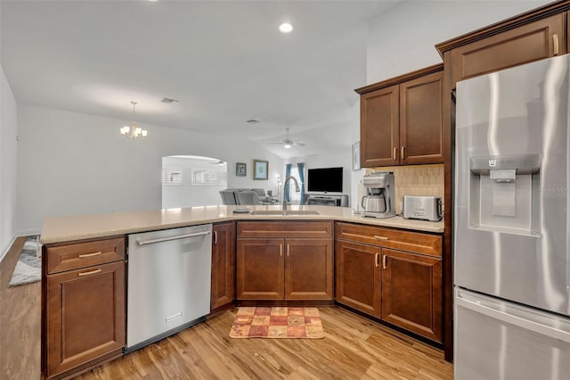 kitchen with kitchen peninsula, sink, light wood-type flooring, appliances with stainless steel finishes, and ceiling fan with notable chandelier