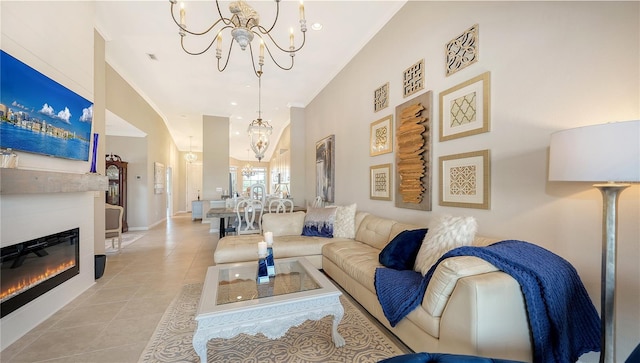 living area featuring baseboards, light tile patterned flooring, a glass covered fireplace, ornamental molding, and a notable chandelier