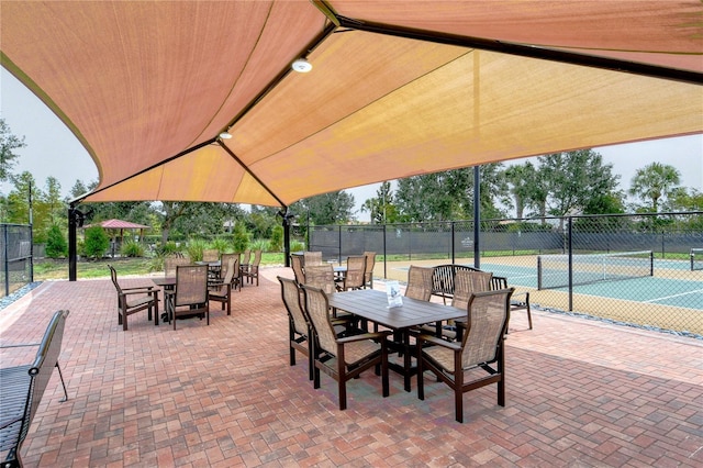 view of patio / terrace featuring a tennis court, outdoor dining area, and fence
