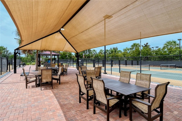 view of patio / terrace with a tennis court, outdoor dining area, a gazebo, and fence