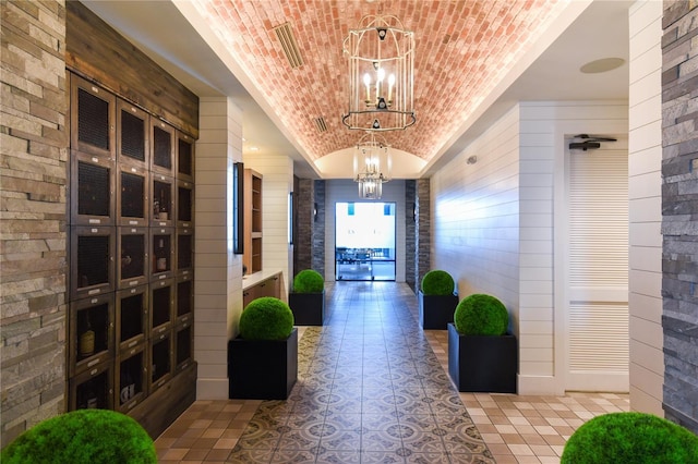 hallway featuring an inviting chandelier, brick ceiling, tile patterned flooring, and vaulted ceiling