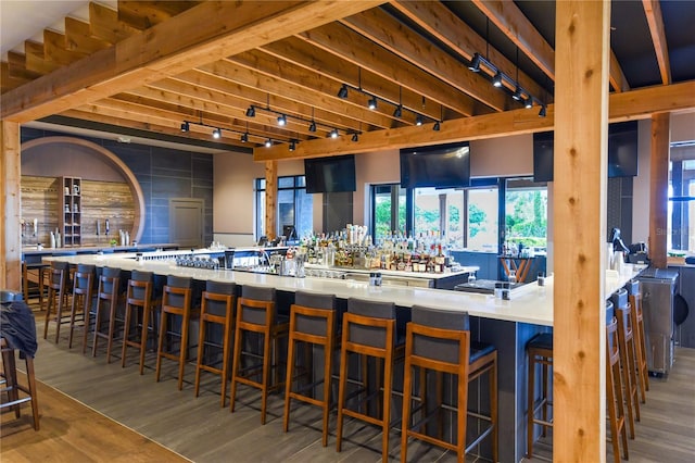 bar with wet bar, rail lighting, beam ceiling, and wood finished floors