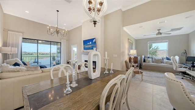 dining area with crown molding, light tile patterned floors, a towering ceiling, a fireplace, and ceiling fan with notable chandelier