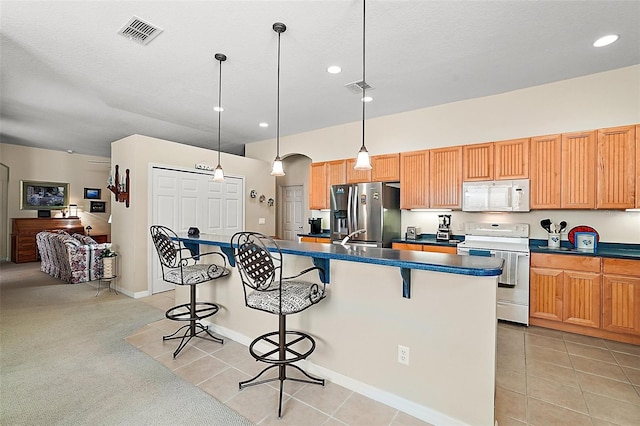 kitchen featuring stainless steel refrigerator with ice dispenser, stove, a kitchen breakfast bar, decorative light fixtures, and a center island with sink