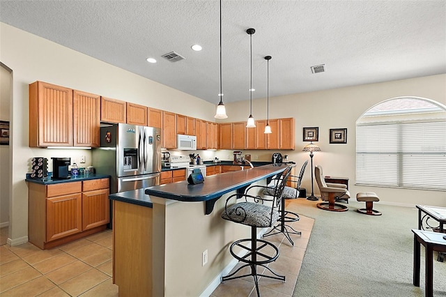 kitchen with hanging light fixtures, a center island with sink, light tile patterned floors, a kitchen breakfast bar, and white appliances