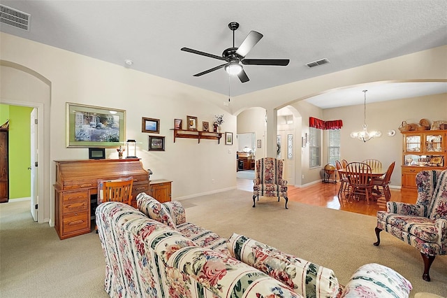 carpeted living room with ceiling fan with notable chandelier and a textured ceiling