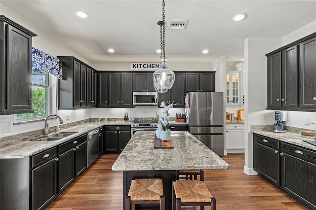 kitchen featuring sink, decorative light fixtures, a center island, light stone counters, and appliances with stainless steel finishes