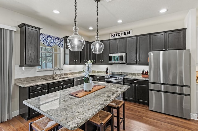 kitchen featuring a breakfast bar area, stainless steel appliances, a center island, light stone counters, and sink