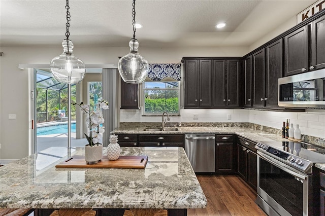 kitchen featuring sink, stainless steel appliances, decorative light fixtures, and a center island