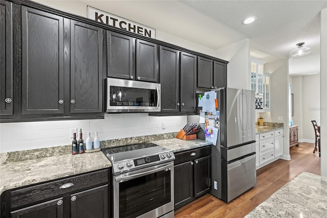 kitchen featuring stainless steel appliances, light stone countertops, hardwood / wood-style flooring, and tasteful backsplash