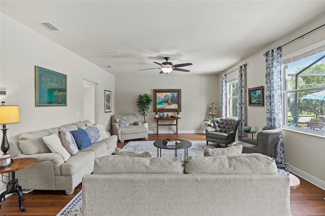 living room with a textured ceiling, ceiling fan, and dark hardwood / wood-style flooring