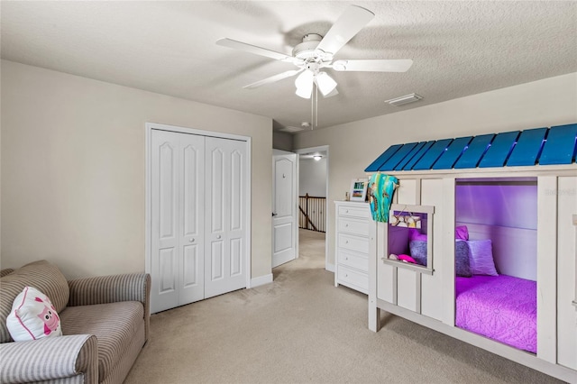 bedroom with a textured ceiling, ceiling fan, a closet, and light carpet