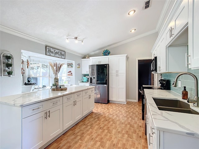 kitchen featuring lofted ceiling, sink, white cabinetry, stainless steel fridge, and light stone counters