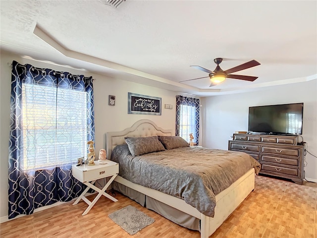 bedroom featuring ceiling fan, a raised ceiling, and light wood-type flooring