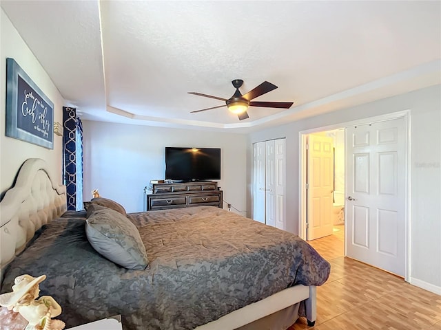 bedroom featuring ceiling fan, a tray ceiling, light hardwood / wood-style flooring, and ensuite bathroom