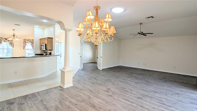 unfurnished room featuring light wood-type flooring, decorative columns, a textured ceiling, ceiling fan with notable chandelier, and vaulted ceiling