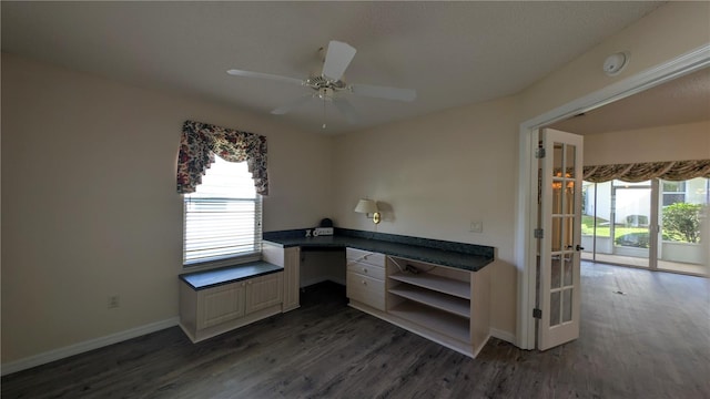 unfurnished office with ceiling fan, dark hardwood / wood-style flooring, built in desk, and a wealth of natural light