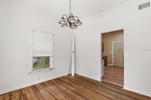 spare room featuring an inviting chandelier and dark hardwood / wood-style floors