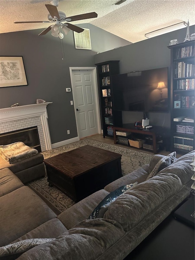 living room with ceiling fan, a textured ceiling, a fireplace, and vaulted ceiling