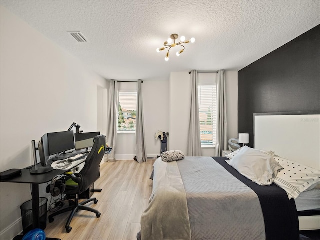 bedroom featuring a textured ceiling, light hardwood / wood-style flooring, a notable chandelier, and multiple windows