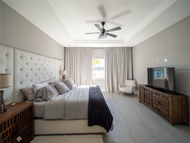 bedroom featuring a raised ceiling, light hardwood / wood-style flooring, a textured ceiling, and ceiling fan