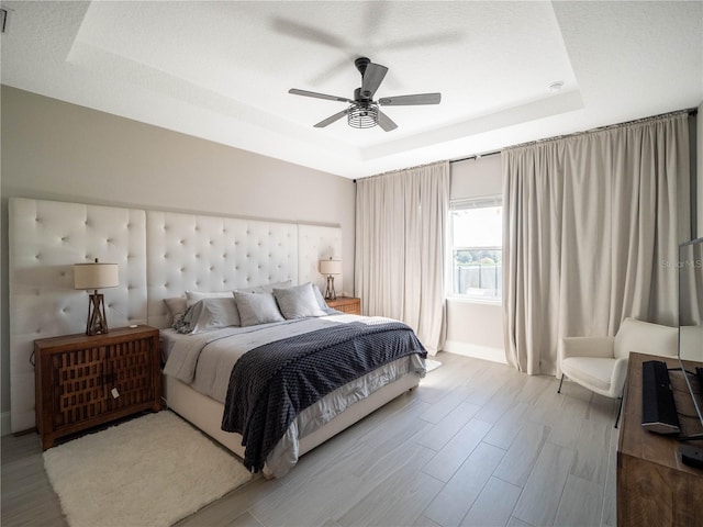 bedroom featuring ceiling fan, wood-type flooring, and a raised ceiling