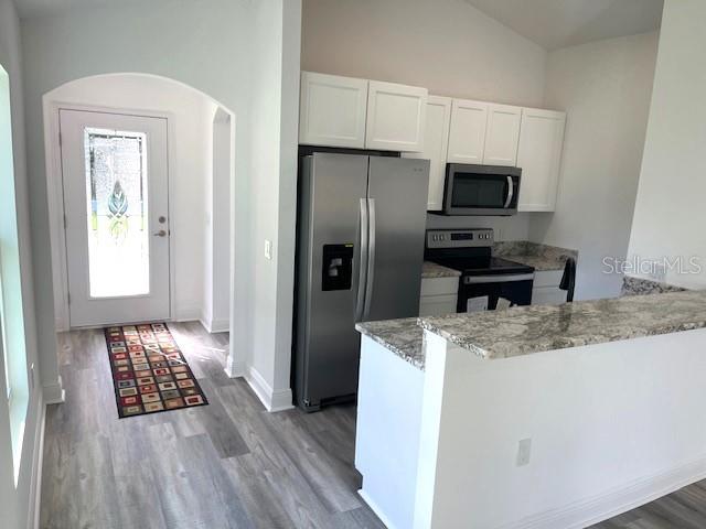 kitchen with appliances with stainless steel finishes, lofted ceiling, white cabinetry, and light hardwood / wood-style floors