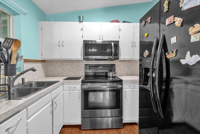 kitchen featuring lofted ceiling, white cabinets, backsplash, sink, and stainless steel appliances